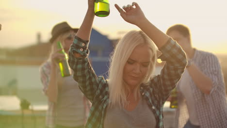 The-Russian-blonde-is-dancing-on-the-roof-with-her-friends-on-the-party.-She-closes-her-eyes-and-moves-her-hands-in-dance-with-beer.